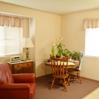 A cozy living room corner with a table, chairs, and potted plants by the windows.