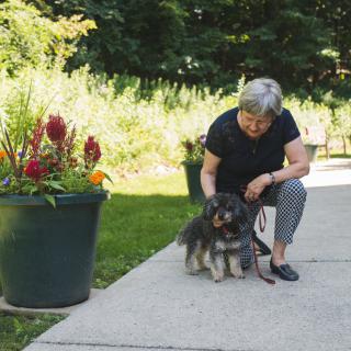 A woman kneels down to pet her dog in a garden setting with vibrant flowers.