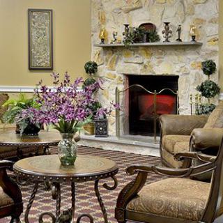 A cozy living room with a stone fireplace, elegant armchairs, and a coffee table adorned with flowers.