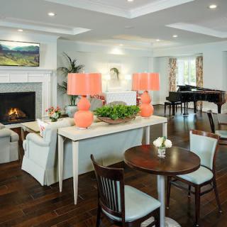 A cozy living room with a fireplace, vibrant table lamps, and a piano in the background.