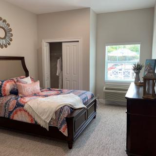 A cozy bedroom with a neatly made bed, window, and dresser.