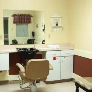 An empty hair salon with a barber chair, mirror, and sink.