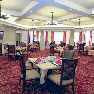 An elegantly decorated dining room with neatly arranged tables and chairs, featuring a red carpet and chandeliers.