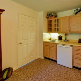A small kitchen area with wooden cabinets, a compact refrigerator, and a carpeted floor.