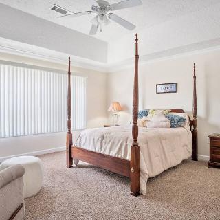 A cozy bedroom featuring a four-poster bed, carpeted floor, and ample natural light through window blinds.