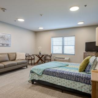 A spacious bedroom with a sofa, bed, and dining area in a well-lit interior setting.
