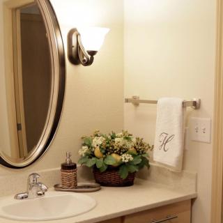 A neatly decorated bathroom featuring a large oval mirror, elegant light fixture, and a floral arrangement next to the sink.