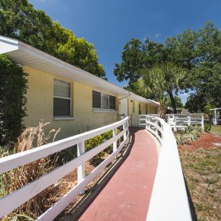 A single-story house with a ramp leading to the entrance, surrounded by trees and greenery.