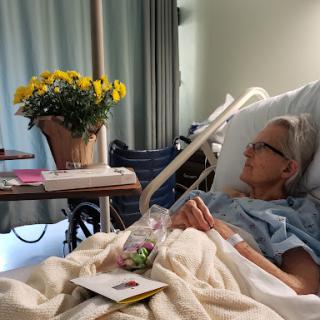 A patient resting in a hospital bed, accompanied by cheerful flowers and personal items.