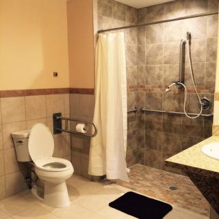 An accessible bathroom featuring a toilet with handrails, a walk-in shower, and a sink.