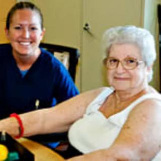 A nurse smiling next to an elderly woman in a healthcare setting.