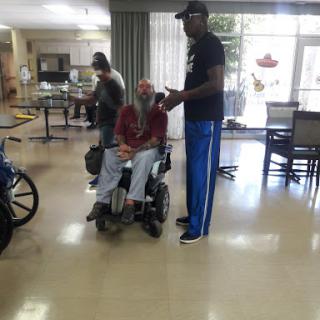 A caregiver provides assistance to an elderly individual in a wheelchair in a rehabilitation facility.