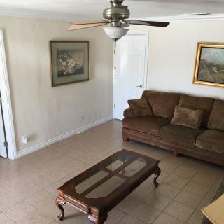 A cozy living room featuring a brown sofa, a glass-top coffee table, and wall-mounted paintings.