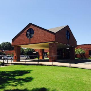 A brick building with a covered driveway and green lawn on a sunny day.