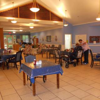 A community dining room with tables, chairs, and people interacting.