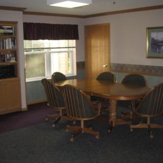 A small conference room with a round table and chairs, featuring a window and bookshelf.