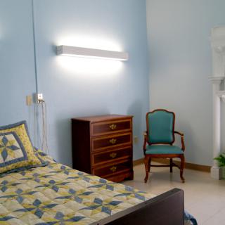 A cozy bedroom with a colorful bedspread, wooden chest of drawers, and an elegant chair.