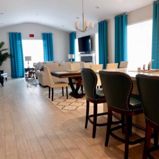 A spacious dining area with elegant furniture and blue curtains, featuring a TV and chandelier.