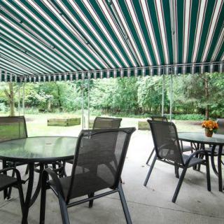 A patio with tables and chairs under a striped awning overlooking a garden.