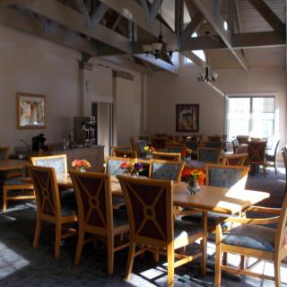 An empty dining area with wooden tables and chairs illuminated by sunlight.