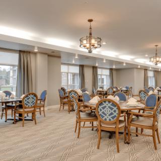 An elegantly decorated dining area with wooden tables and chairs, soft lighting from chandeliers, and large windows.