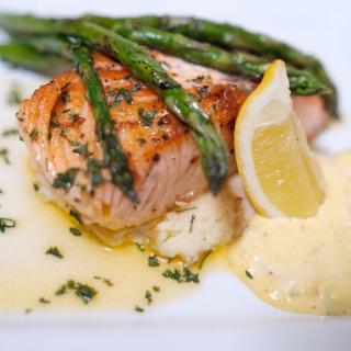 Grilled salmon served with asparagus, lemon, and creamy sauce.