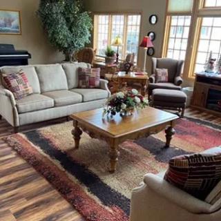 A cozy living room featuring a sofa, coffee table, armchair, and piano near large windows.