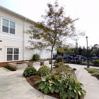 A well-landscaped apartment building exterior with a tree and plants lining the pathway.