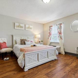 A cozy bedroom featuring a large bed with decorative pillows, a wooden floor, and natural light streaming in through a window.