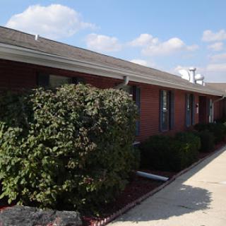 A well-maintained brick building with lush greenery in front under a blue sky.