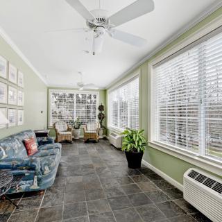 A bright sunroom featuring large windows, comfortable seating, and decorative plants.
