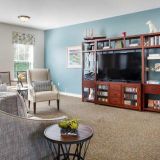 A cozy living room featuring a large TV on a wooden entertainment center, with comfortable seating and stylish decor against a blue accent wall.