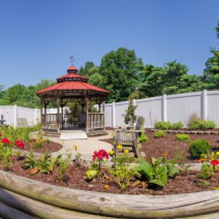 A serene garden featuring a beautiful gazebo surrounded by vibrant flowers and a clear blue sky.