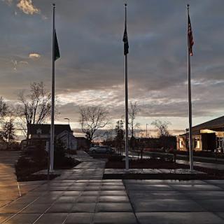 Three flagpoles stand silhouetted against a cloudy sunset sky near buildings.