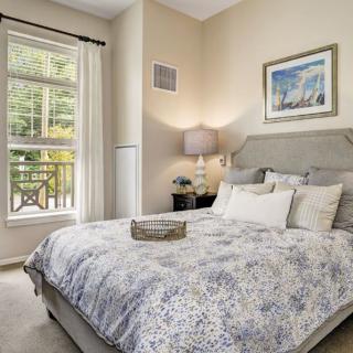 A cozy bedroom with elegant bedding, decorative artwork, and a large window.