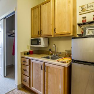 A compact kitchen area featuring wooden cabinets, a microwave, a small refrigerator, and a sink.