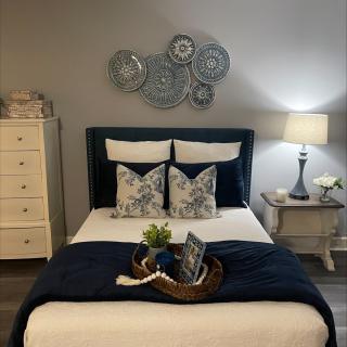 A cozy, well-decorated bedroom featuring a bed with decorative pillows and a blanket, a nightstand with a lamp, and wall art.