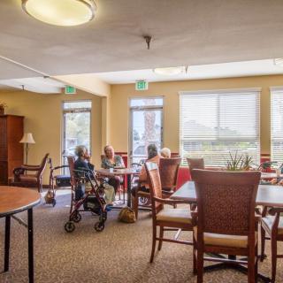 A bright and welcoming interior of a nursing home with residents sitting around tables.