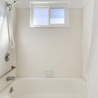 A minimalist bathroom with a bathtub and shower, featuring white walls and a window.