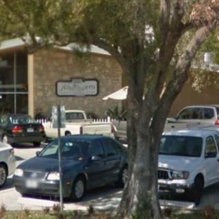 A small parking lot in front of a building with several parked cars and a large tree.