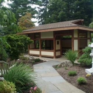 A serene Japanese garden featuring a wooden pavilion and a stone pathway surrounded by lush greenery.
