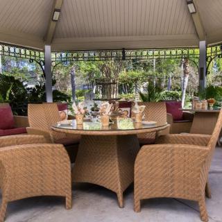 A cozy outdoor seating area under a gazebo with wicker chairs and a well-set table.