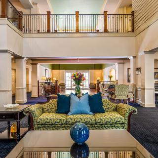 A stylish and inviting lobby featuring a patterned sofa with colorful pillows, a decorative vase on the coffee table, and an open mezzanine in the background.