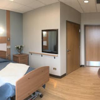 A modern hospital room with a bed, chair, and entrance.