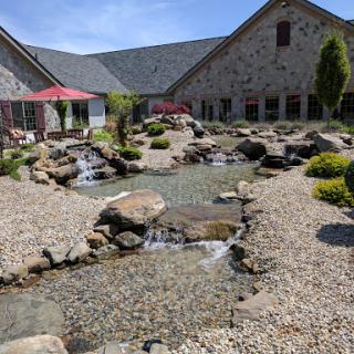 A beautifully landscaped garden featuring a serene water stream, smooth stones, and a picturesque building in the background.