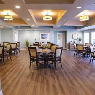 A modern dining area with neatly arranged tables and chairs, featuring warm lighting and a wooden floor.