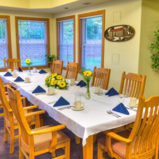 A well-decorated dining room with a long table set for a gathering, featuring sunflowers and neatly folded blue napkins.
