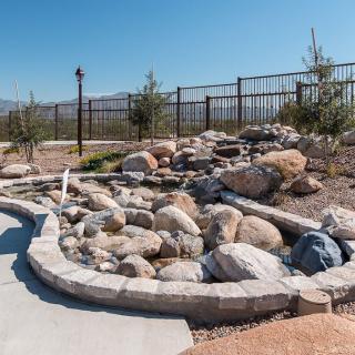 A landscaped garden featuring a rock arrangement with surrounding trees and fencing.