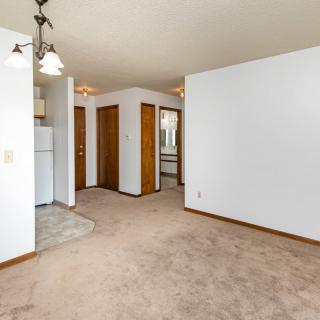 An empty living room with carpeted flooring, white walls, and several doorways.