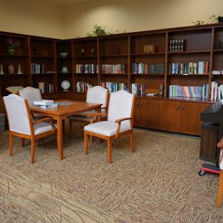 A cozy corner of a library or office featuring wooden bookshelves filled with books, a wooden table, and white upholstered chairs.